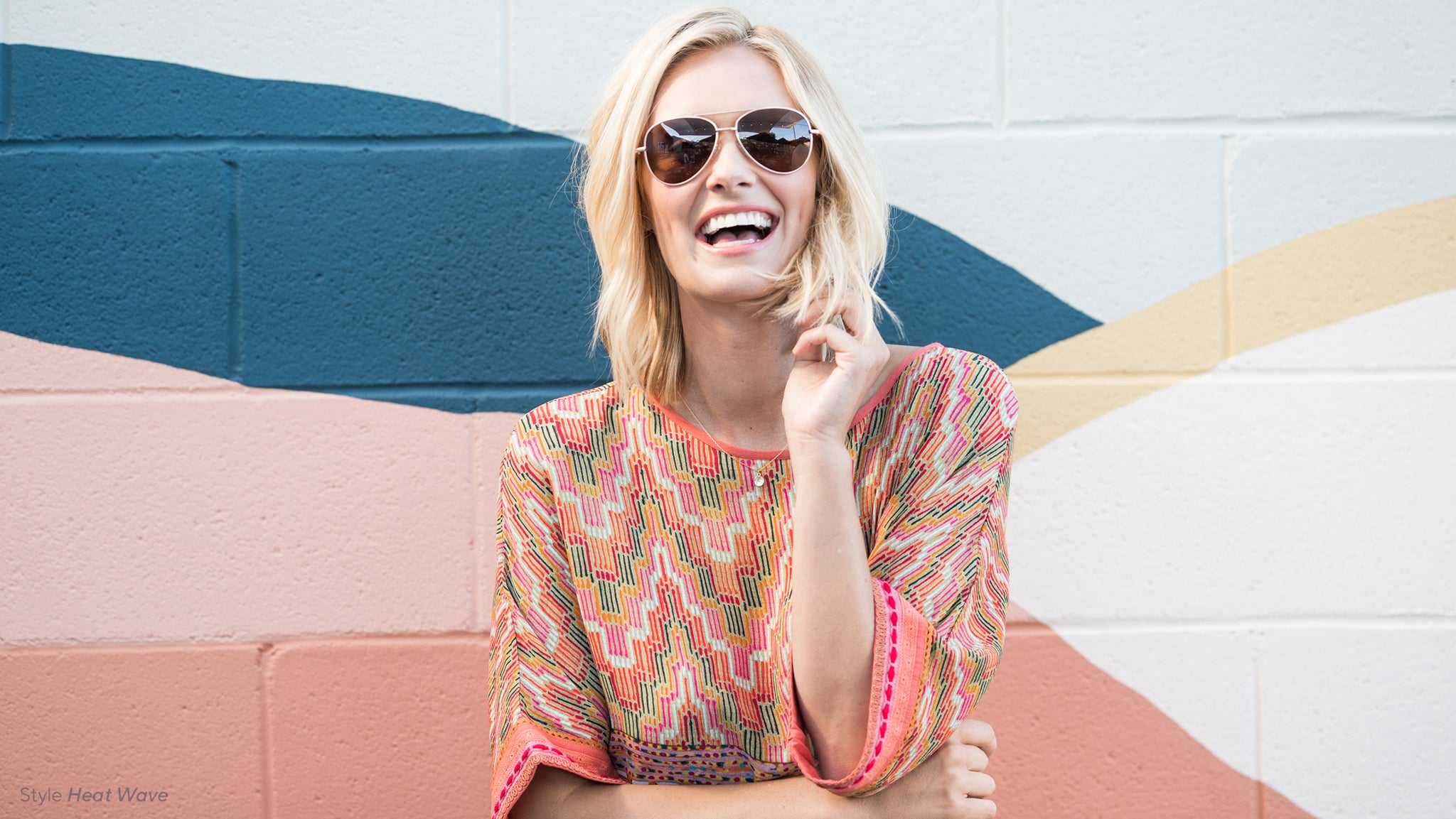 Blonde woman laughing in front of mural wearing Peepers Heat Wave sunglasses