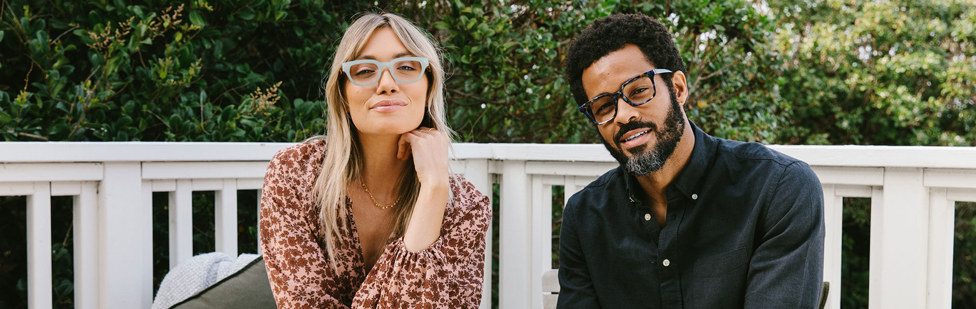 Man and woman sitting on deck looking at camera. Woman is wearing Peepers Blue Light Style Flora and man is wearing Peepers Reading Glasses Bowie