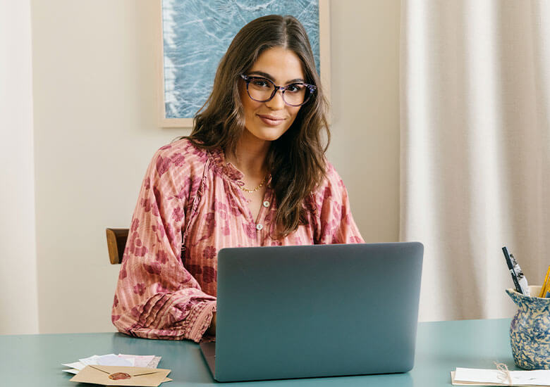 Woman in Peepers Blue Light Glasses Monarch Sitting at Desk In Front of Computer