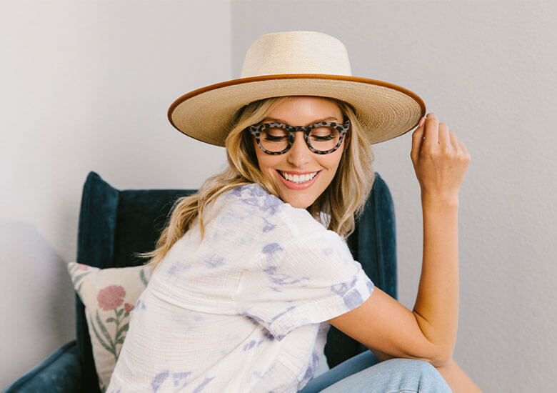 Woman Sitting in Chair with Wide Brim Sunhat on Wearing Stardust Reading Glasses