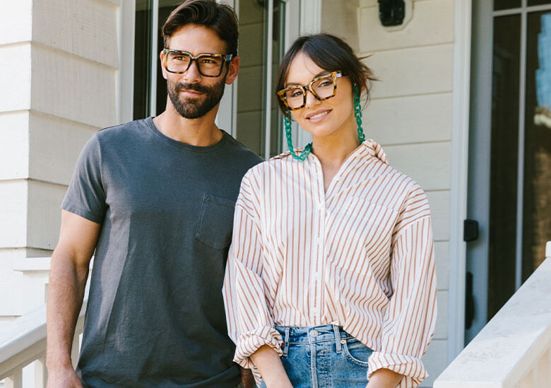 Woman and man standing outside on a deck next to each other. Woman wearing Peepers Reading Glasses Sterling and man wearing Peepers Blue Light Glasses Vaughn