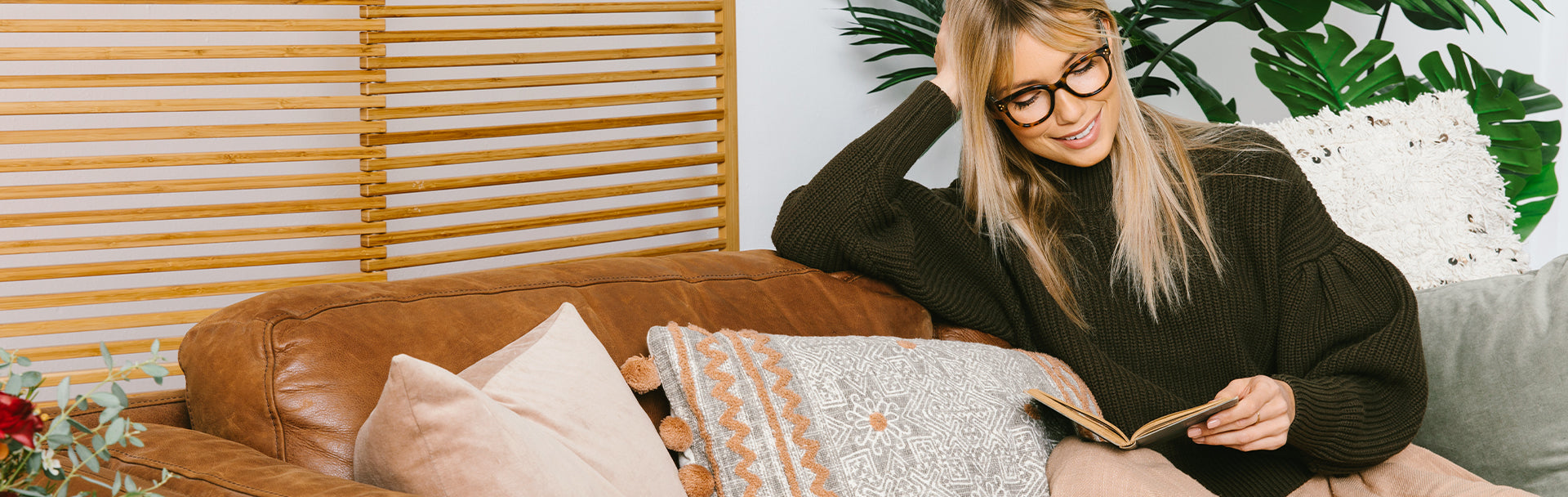 Blonde woman wearing Peepers reading glasses and reading a book on the couch