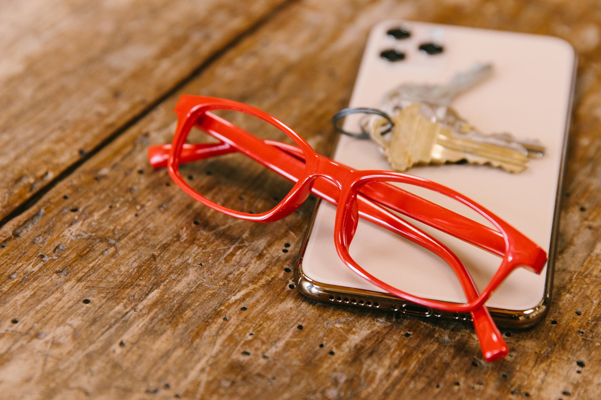 Peepers red reading glasses sitting on a phone and keys