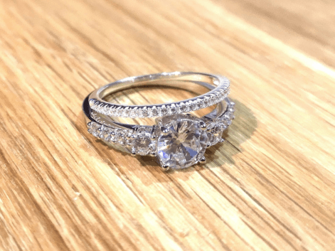 A 3 stone diamond engagement ring and a diamond eternity ring on a wooden table