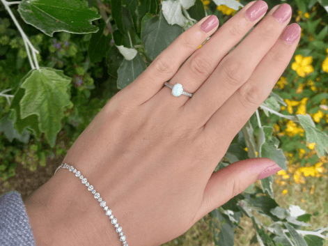 Woman wearing an oval opal ring and cz tennis bracelet on a floral background