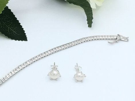 Pearl earrings and a channel set diamond tennis bracelet on a white background