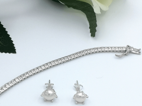 Silver tennis bracelet with pearl earrings on a white background