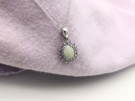 oval cut opal & tanzanite halo necklace on a purple napkin