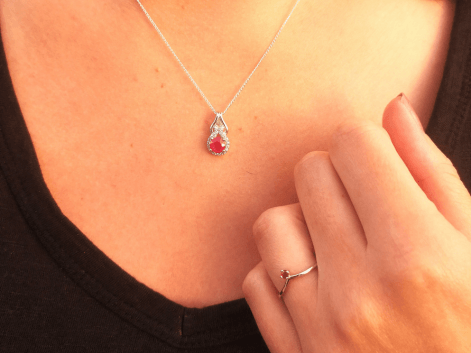 woman wearing a ruby & cz halo pendant and a solitaire ruby wishbone ring