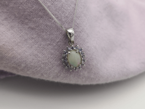 an oval opal and tanzanite halo pendant on a purple napkin