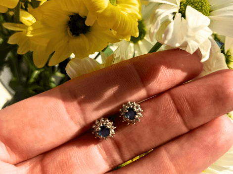 woman holding a pair of sapphire and cz stud earrings next to a yellow flower