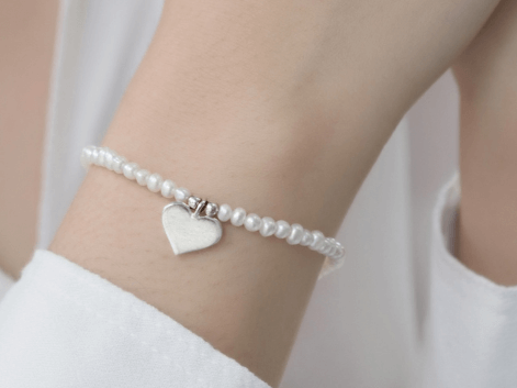 A woman wearing a beaded pearl heart charm bracelet