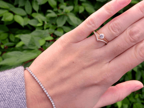 Woman wearing a 14kt gold plated ring stack with a silver cz tennis bracelet on a floral background
