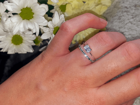 Woman wearing a baguette cut diamond solitaire engagement ring with a diamond eternity ring on a floral background