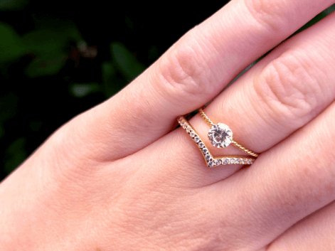 Woman wearing a gold solitaire diamond ring and a gold diamond wishbone wedding band