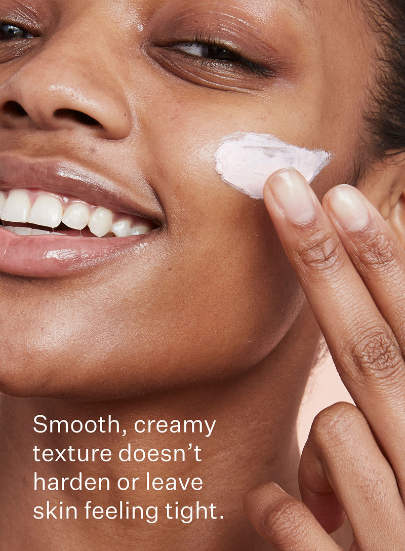 A young woman applies a thin layer of clay mask for pores to her cheek with a smile with a highlight of how the smooth, creamy texture of the product doesn't harden or leave the skin feeling tight