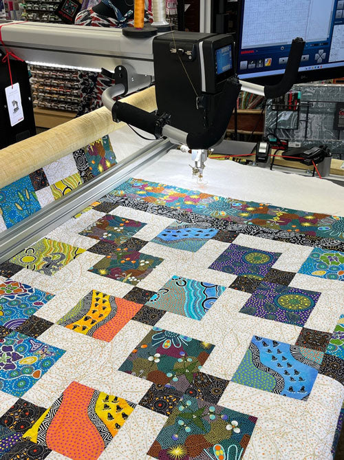 Australian fabric Disappearing 9 Patch quilt with borders being longarm quilted