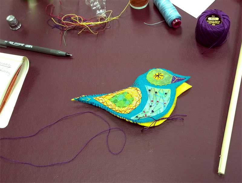 Felt and fabric bird front embellished with hand stitching being whipstitched together with its back