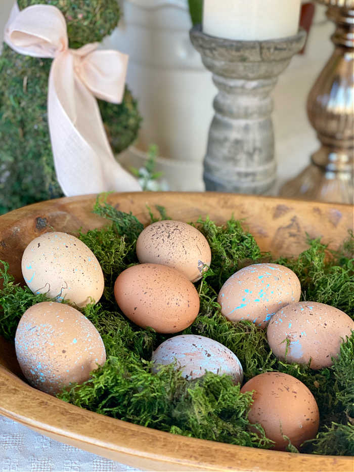 Splatter painted brown blown eggs in a wooden bowl with moss