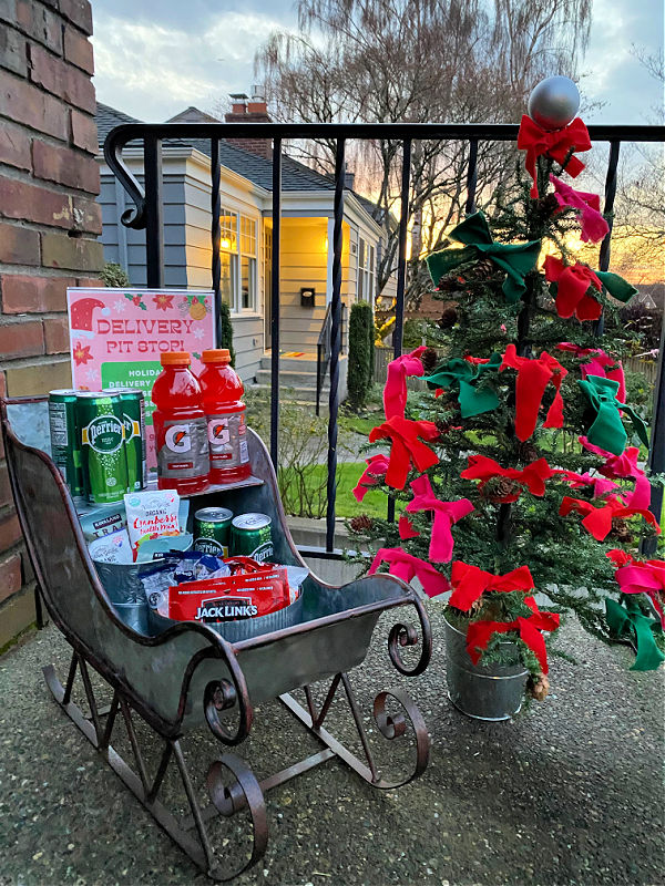 Photo of small metal sleigh on porch stocked with snacks next to a small faux Christmas tree