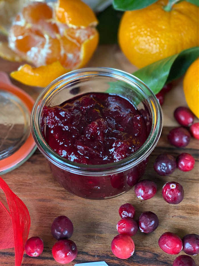 Orange cranberry sauce in a clear jar with berries and oranges surrounding