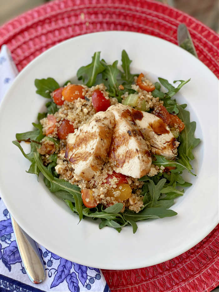 Sliced chicken on top of quinoa salad and arugula leaves