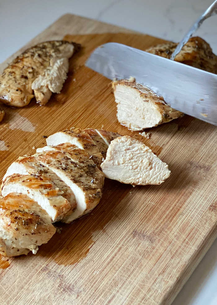 Chef's knife and tongs cutting herbed chicken breast on bamboo cutting board