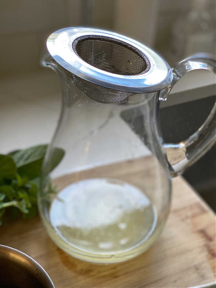 photo of a small strainer on the top of a clear glass pitcher with lemon juice in the bottom