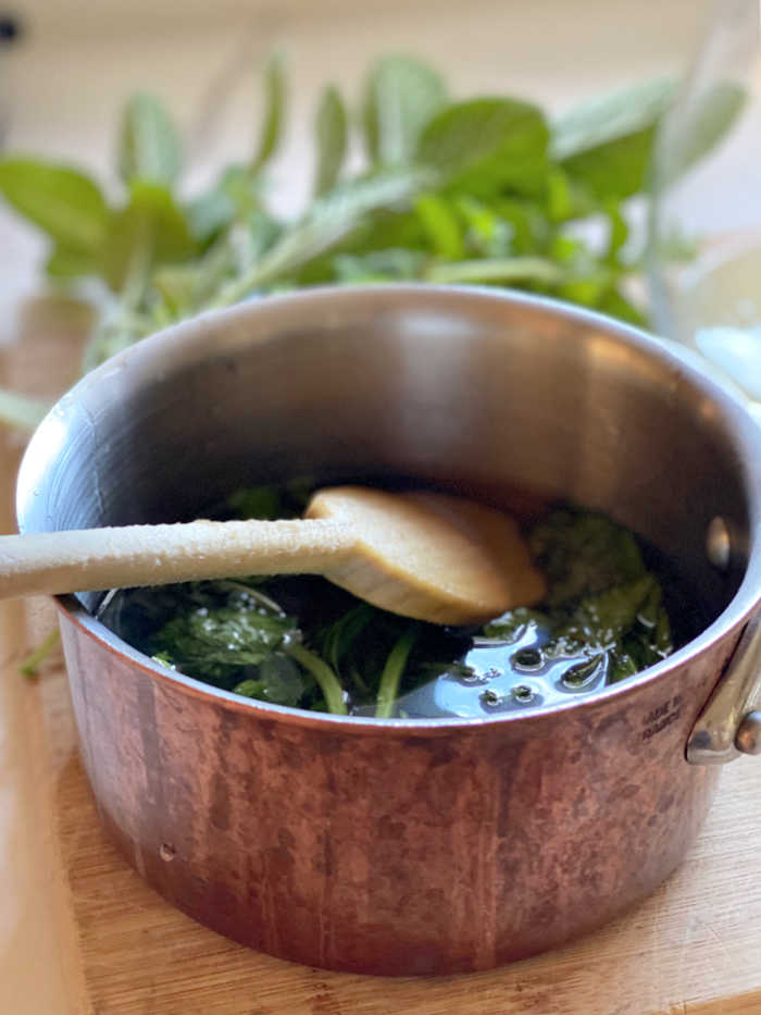 Photo of herbs in a saucepan with water and sugar and a wooden spoon