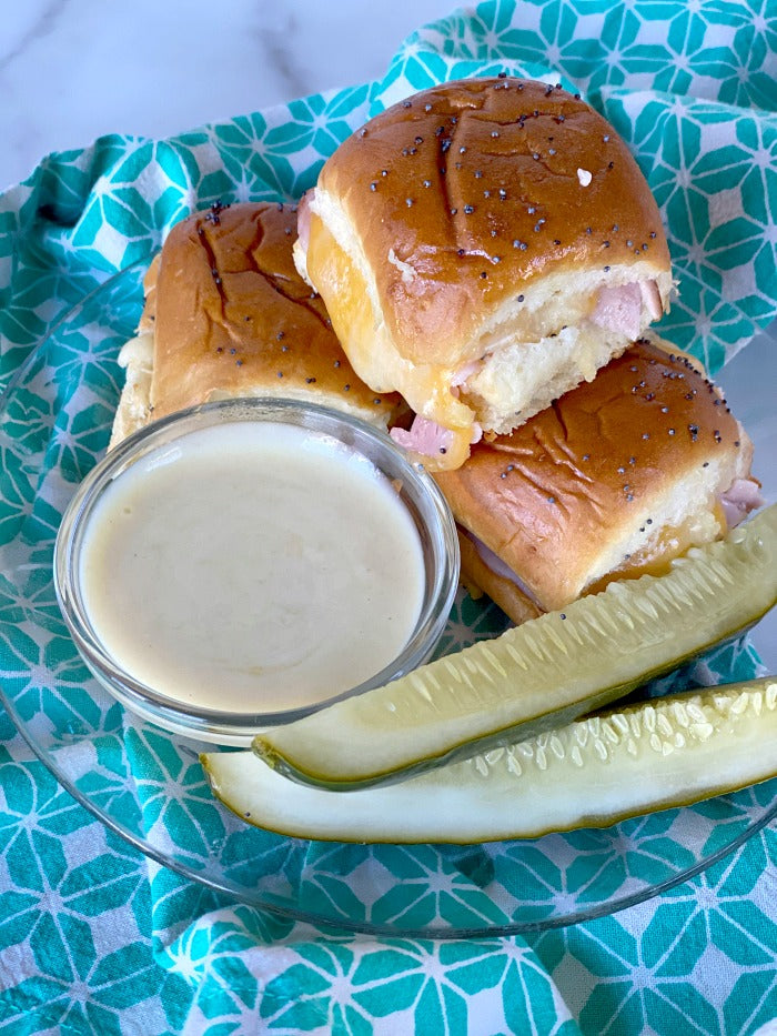 Ham and cheese sliders on Hawaiian rolls with honey mustard dipping sauce. This easy recipe makes great game day food and busy weekday lunch fare. I make these once per week during #distancelearning #covid19 #easyrecipes #lunch #20minuterecipe #sliders #football #potluck #partyfood