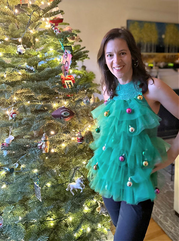 photo of woman standing by a Christmas tree in tree top ornament ugly sweater