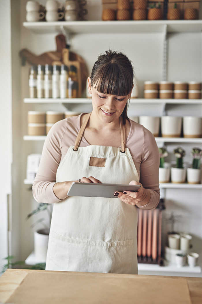 Woman in apron working on ipad planning promotional events for Q4