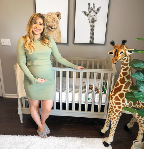 pregnant woman standing in front of a crib in a safari themed baby boy nursery