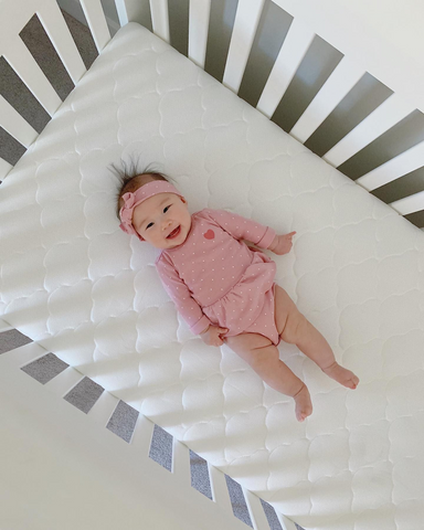 smiling baby laying on crib mattress