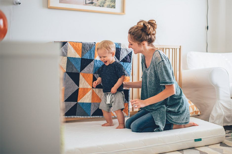 Mom with toddler in nursery walking on crib mattresss