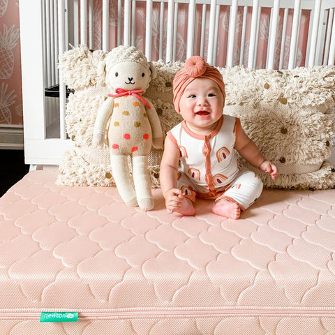 baby sitting on a bed with a stuffed animal