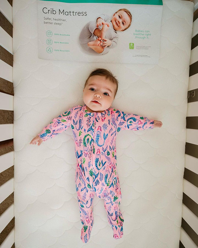 baby in a sleep sack laying in a crib