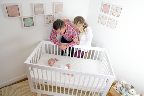 Parents looking down at sleeping baby in crib