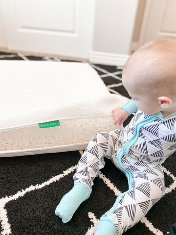 Baby sitting next to a breathable crib mattress