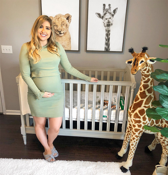 Expecting mom standing next to crib in zoo themed nursery