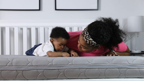 Baby laying on stomach on mattress with mom