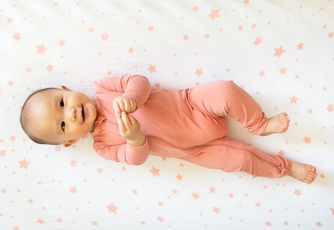 baby in pink onesie laying on back 