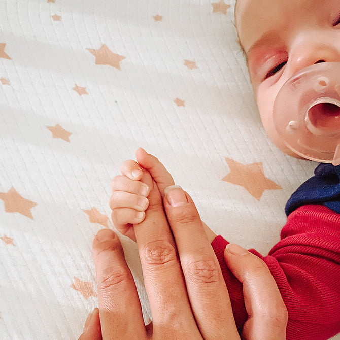 baby holding parents finger while falling asleep