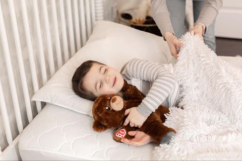 Young kid being tucked in for sleep while holding his teddy bear