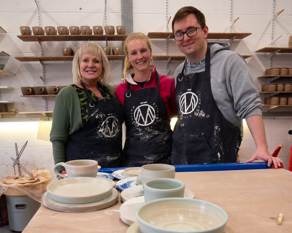 Photo from a pottery workshop with three smiling people and their hand made pots.