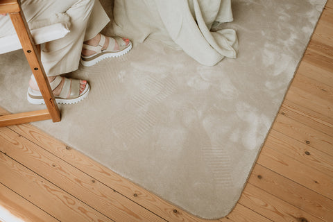Bovenaanzicht duurzaam tapijt op parket vloer en schoenen van zittende vrouw in rieten stoel.
