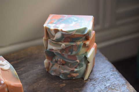 Stack of Almost Autumn handmade soaps on a wooden stool in daylight