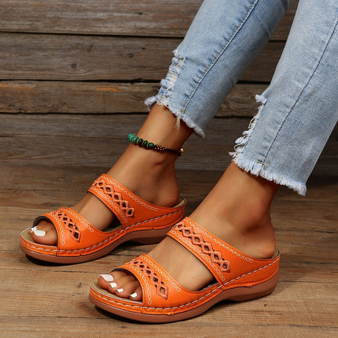 Eine Nahaufnahme der Füße einer Person, die orangefarbene Sandalen und hellblaue Distressed-Jeans trägt.