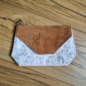 Pochette artisanale posée sur un sol en bois, composée d’un rabat en velours côtelé marron et d’un tissu en coton à motif floral discret dans des tons doux. Accessoire cousu main idéal pour ranger stylos, maquillage ou petits objets. Design élégant et naturel, parfait pour un usage quotidien ou à offrir.