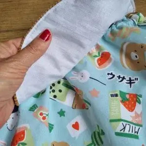 Zoom sur l’intérieur d’un sac à dos pochon fait main, montrant la doublure blanche en coton et le tissu extérieur bleu à motifs kawaii (lapin, ours, fraise, bubble tea, écritures japonaises). Finition soignée, idéale pour un sac enfant personnalisé et confortable.